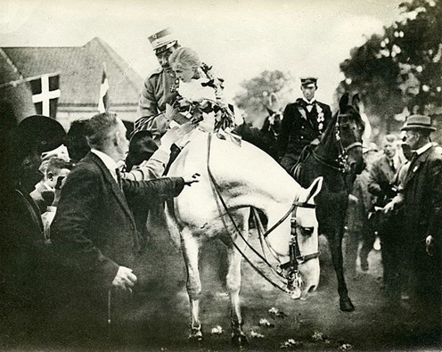 “Genforeningen 1920 Chr X på hest med en pige - Fra Genforeningen 1920 Chr. X på hest med pigen Elisabet Braren Arkiv: Kolding Stadsarkiv”, licenseret under CC-zero. 